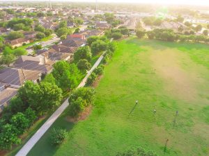 Aerial huge park near residential houses with people playing sport, exercising on green meadow. Green urban recreation surrounds by green tree in Houston, Texas, US.. Tightly packed homes neighborhood